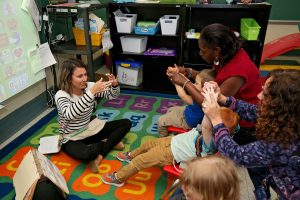 Teacher sitting on the floor demonstrating a song to young students in a circle