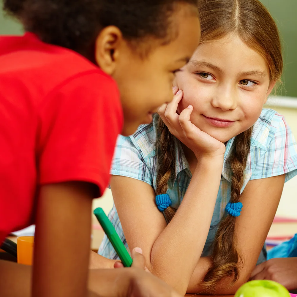 Teaching Critical Communication Skills Online Workshop Two girls whispering, classroom.